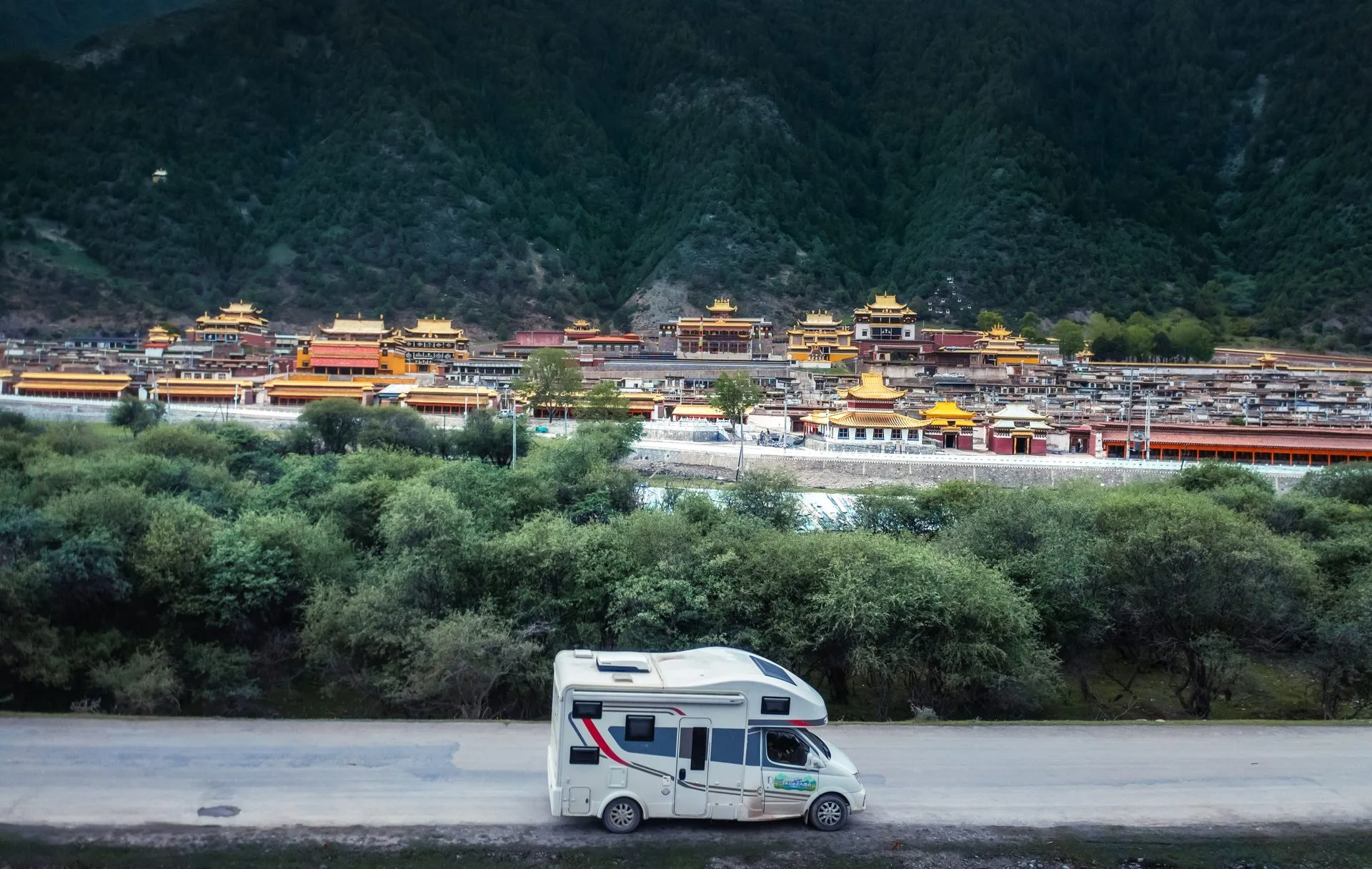 Campervan parked in front of Gongba Monastery surrounded by forests in Qinghai-Gansu, China